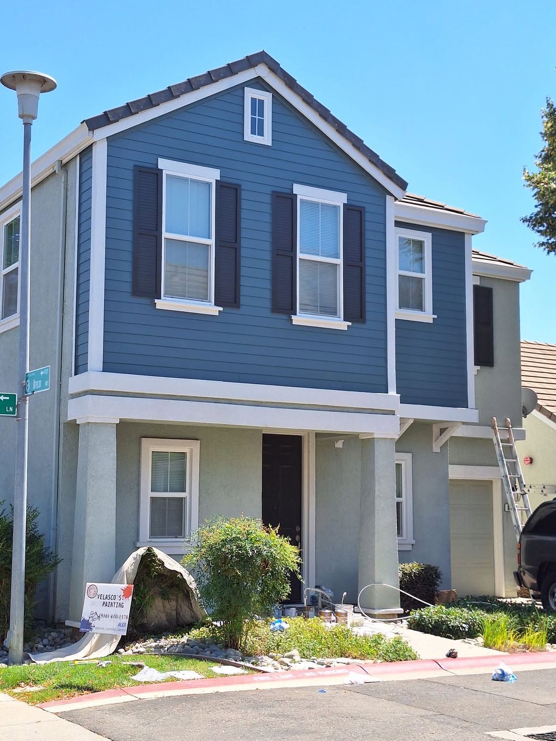 Deep blue two-story siding repaint with Velasco's Painting sign on site